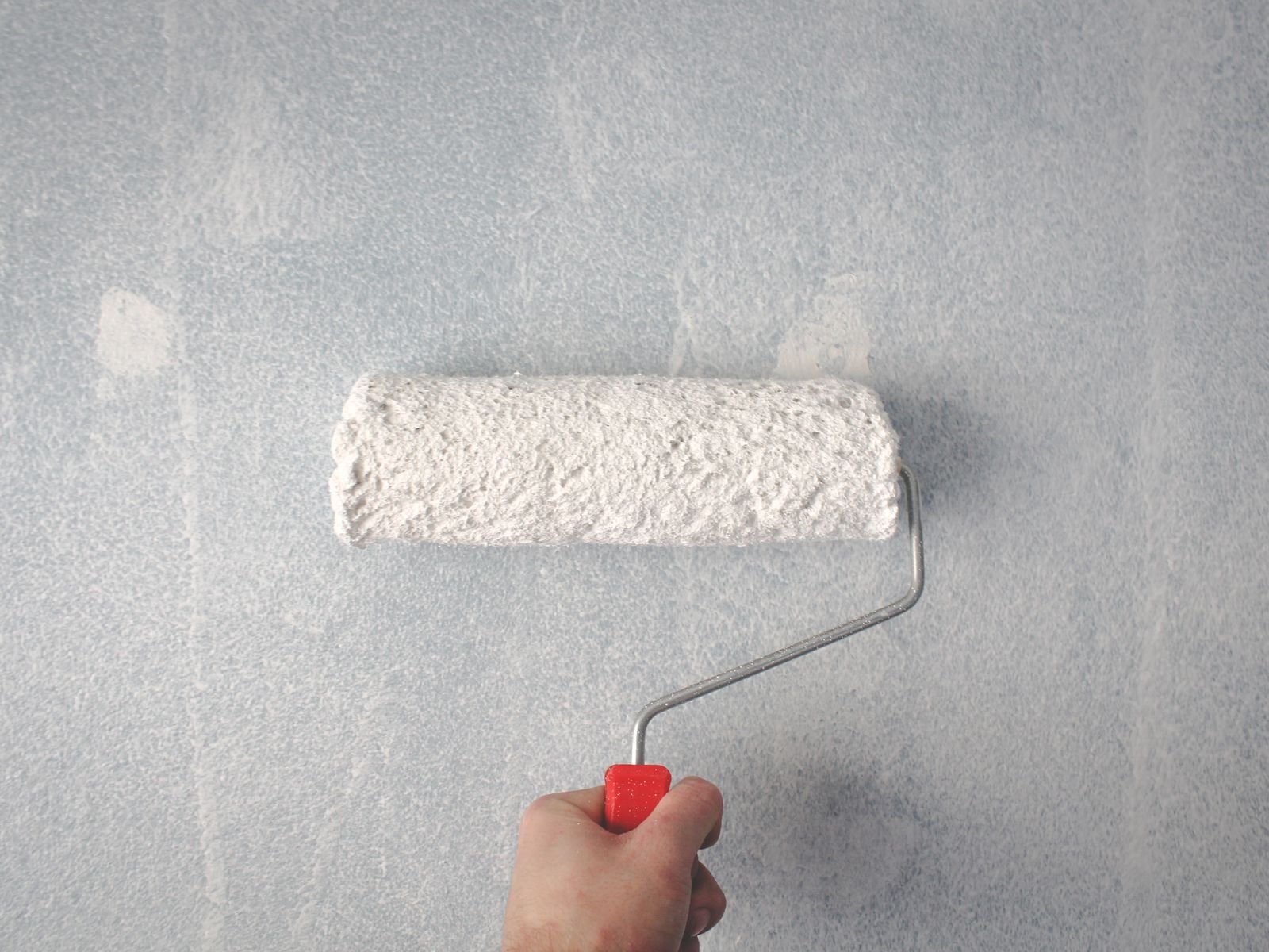 Roller applying a fresh coat of white paint to an interior wall